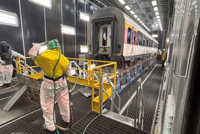 Fase di sabbiatura industriale su manufatti ferroviari con operatore dotato di dispositivi di protezione.